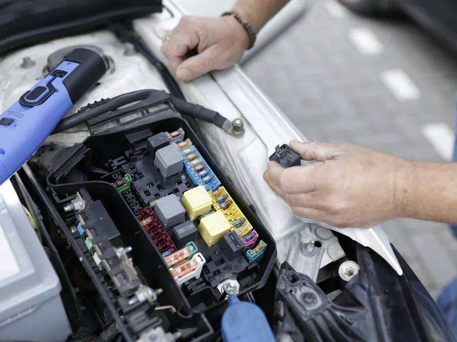 Mechanic's hands checking a relay at a car's under-hood fuse box