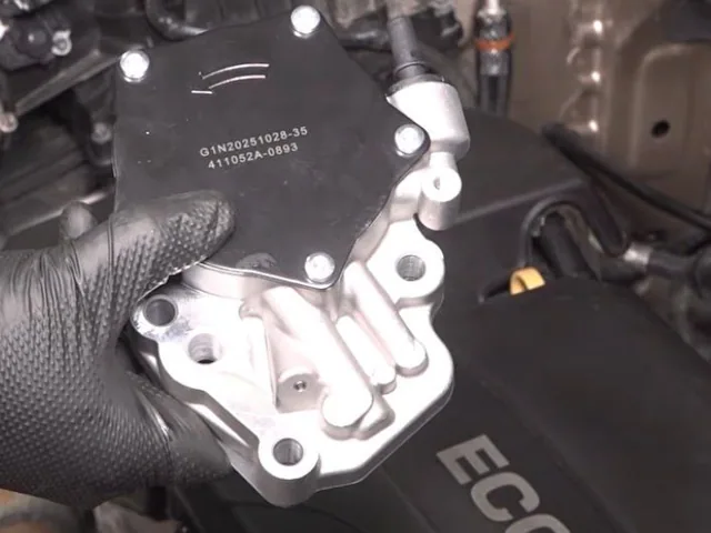 Gloved hand holding a new replacement engine part over a car's engine bay