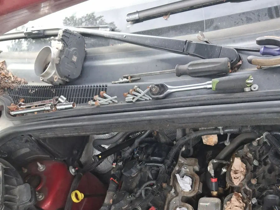 Tools laid out along the cowl of a car with its engine opened up for repair