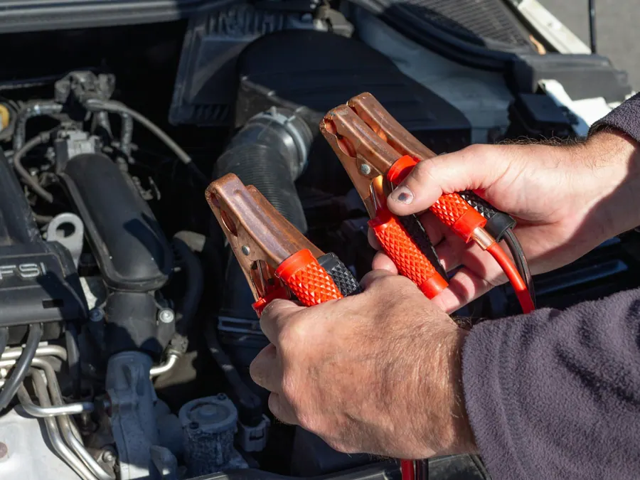 Hands holding jumper cable clamps over a car's engine bay